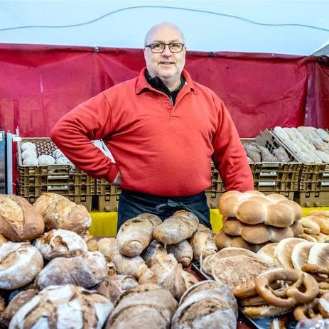 Willem achter de kraam met bruinbrood, desembrood, bollen en krakelingen.